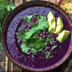 Bowl of purple black bean soup with garnishes and cornbread.